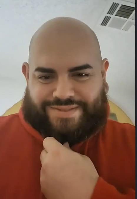 A bald, Caucasian male with a dark beard in red shirt smiling mischievously
